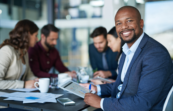 An African American businessman smiles while seated at a table with colleagues, promoting teamwork and positive interactions