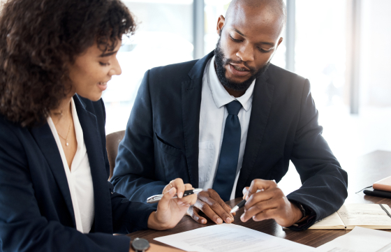 Two business professionals engaged in discussion at a table, surrounded by documents and papers, focused on their work.